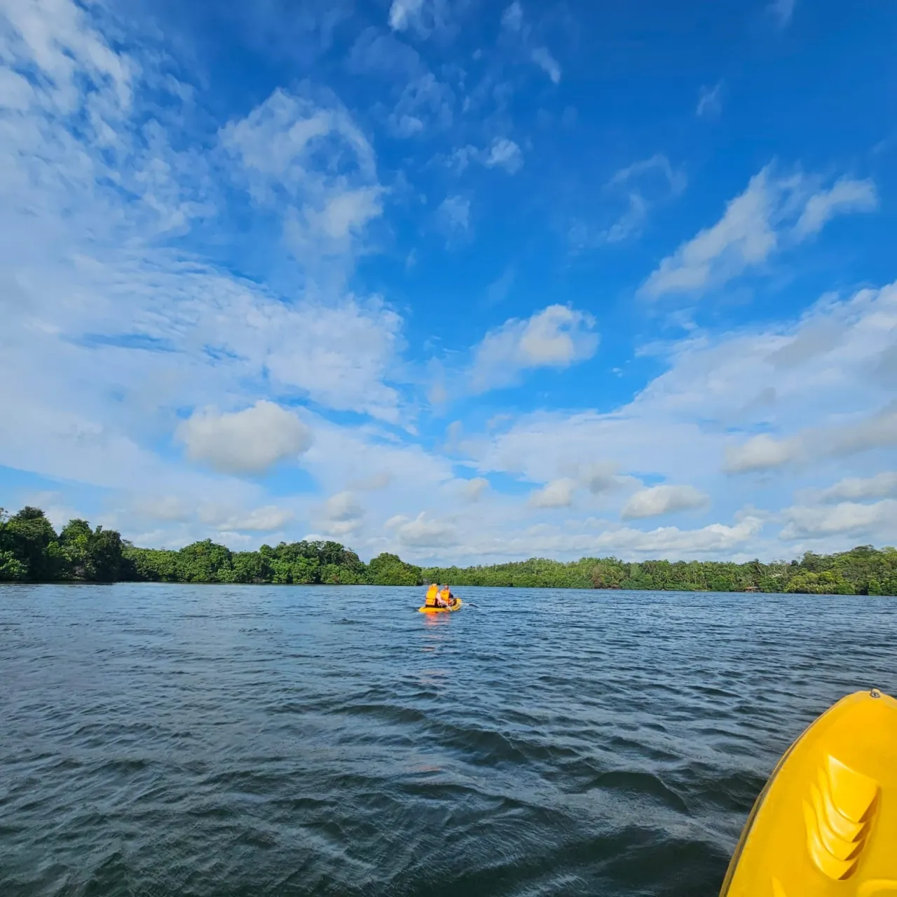 Couple paddling a yellow tandem kayak in the distance on Rathgama Lagoon under a bright blue sky