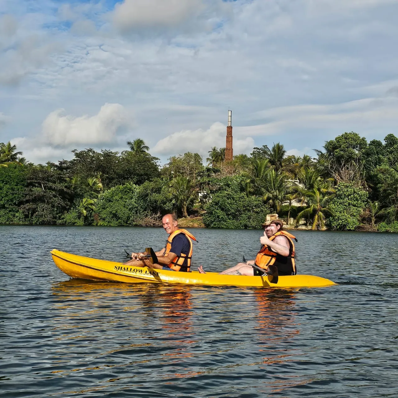 Two smiling men giving a thumbs up while kayaking in a yellow kayak on Rathgama Lagoon