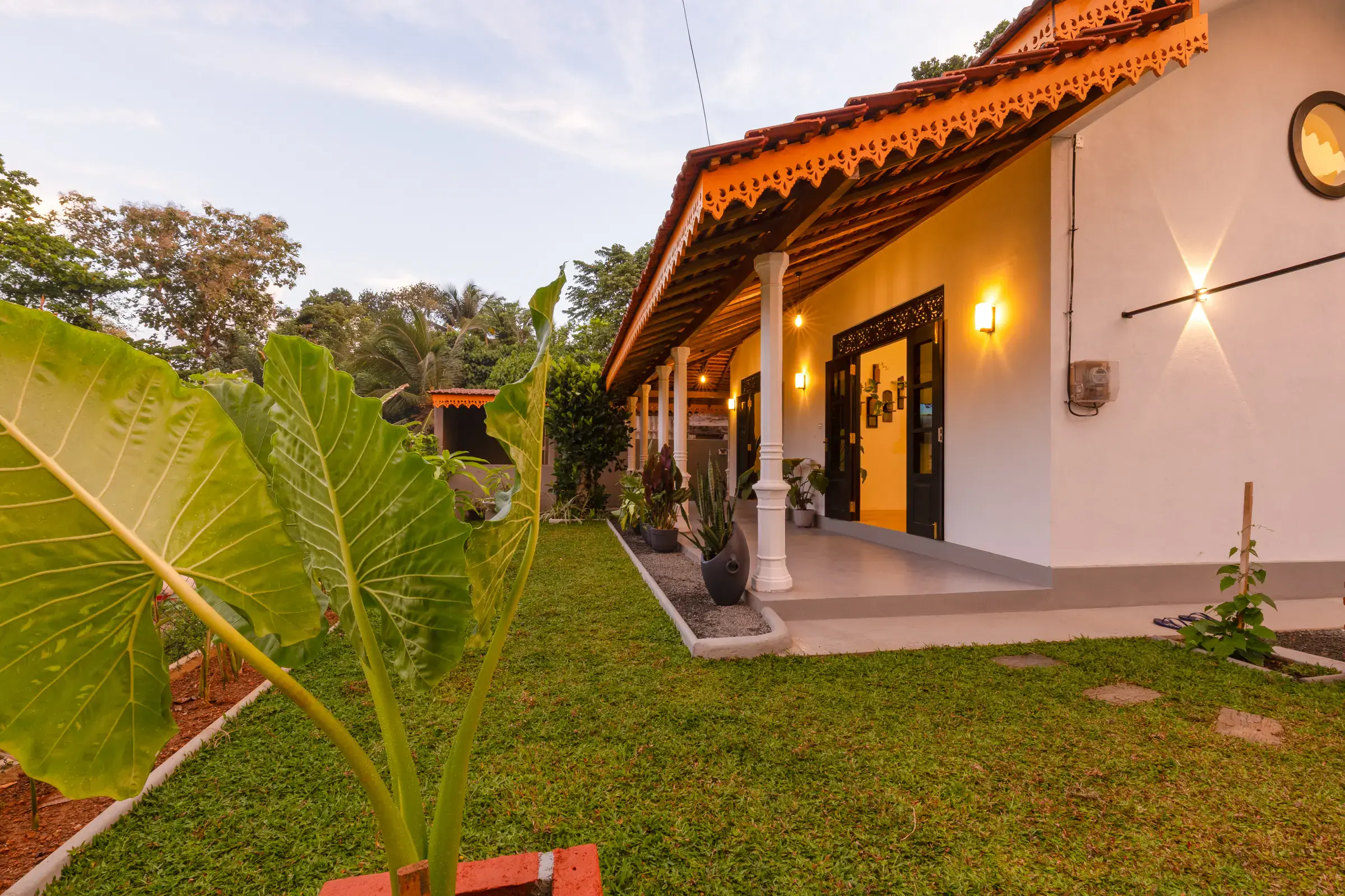 Lush private tropical garden with Alocasia plants and warmly lit villa veranda at Serene Luxe