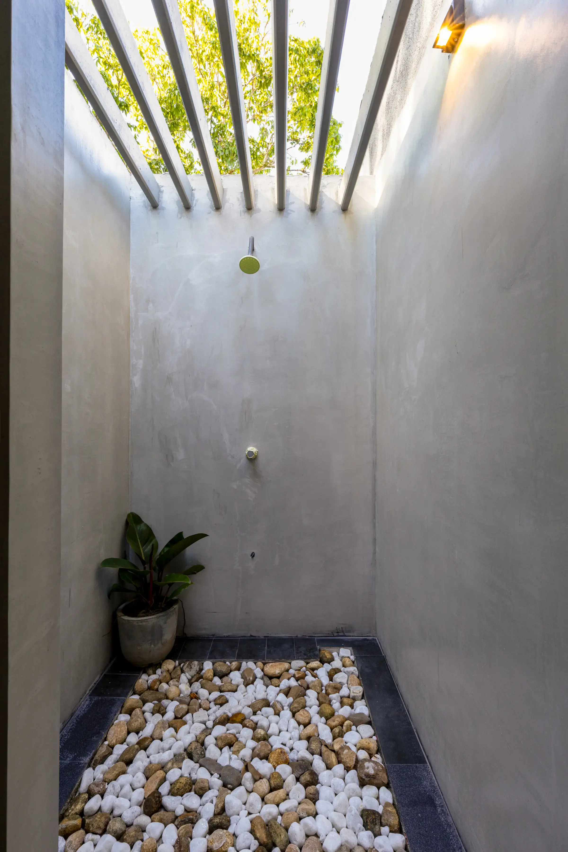 Open-air outdoor shower with concrete walls, river stone floor and natural light at Serene Luxe Villa