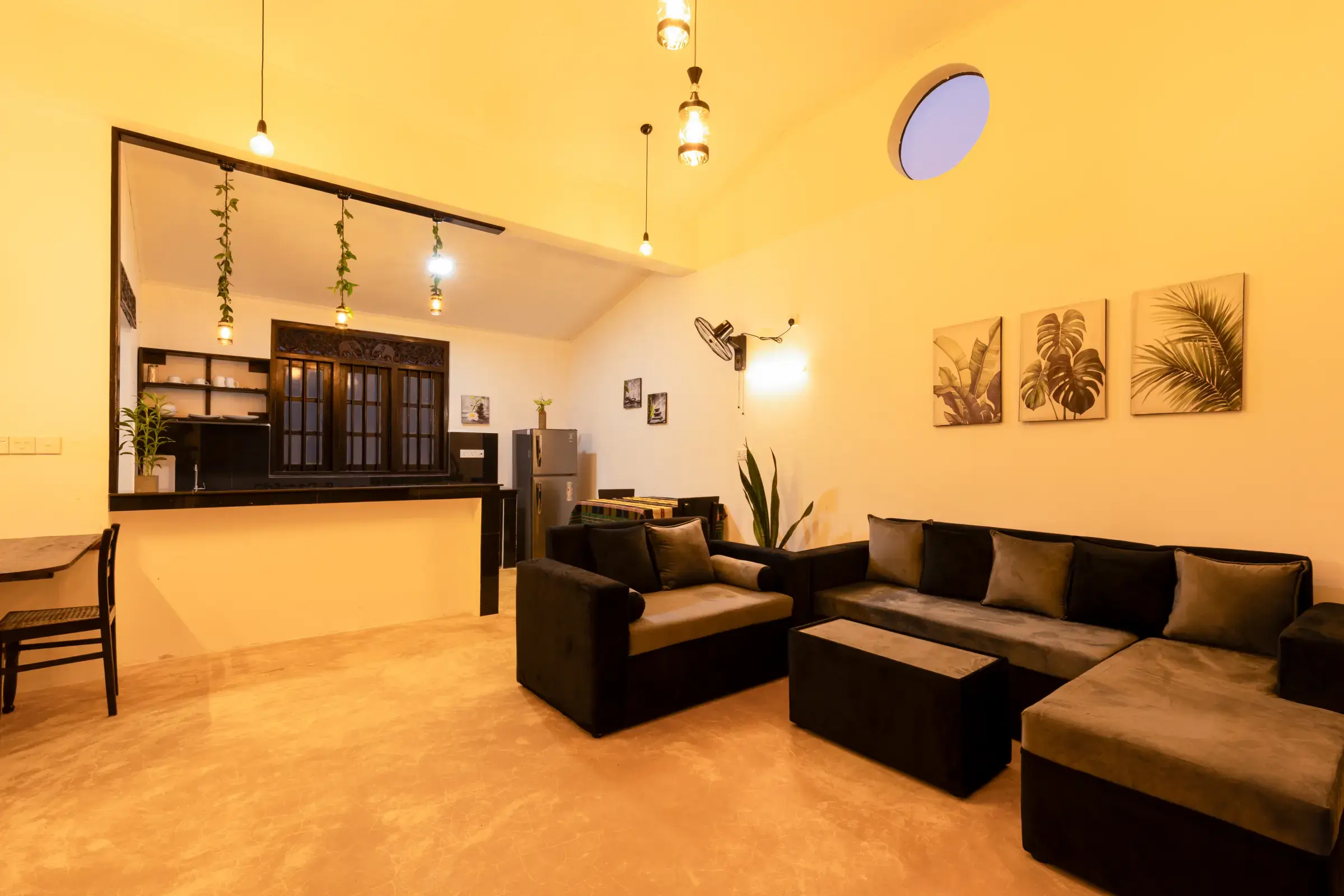 Private open-plan living room and kitchen with dark sofas and round skylight at Serene Luxe Villa
