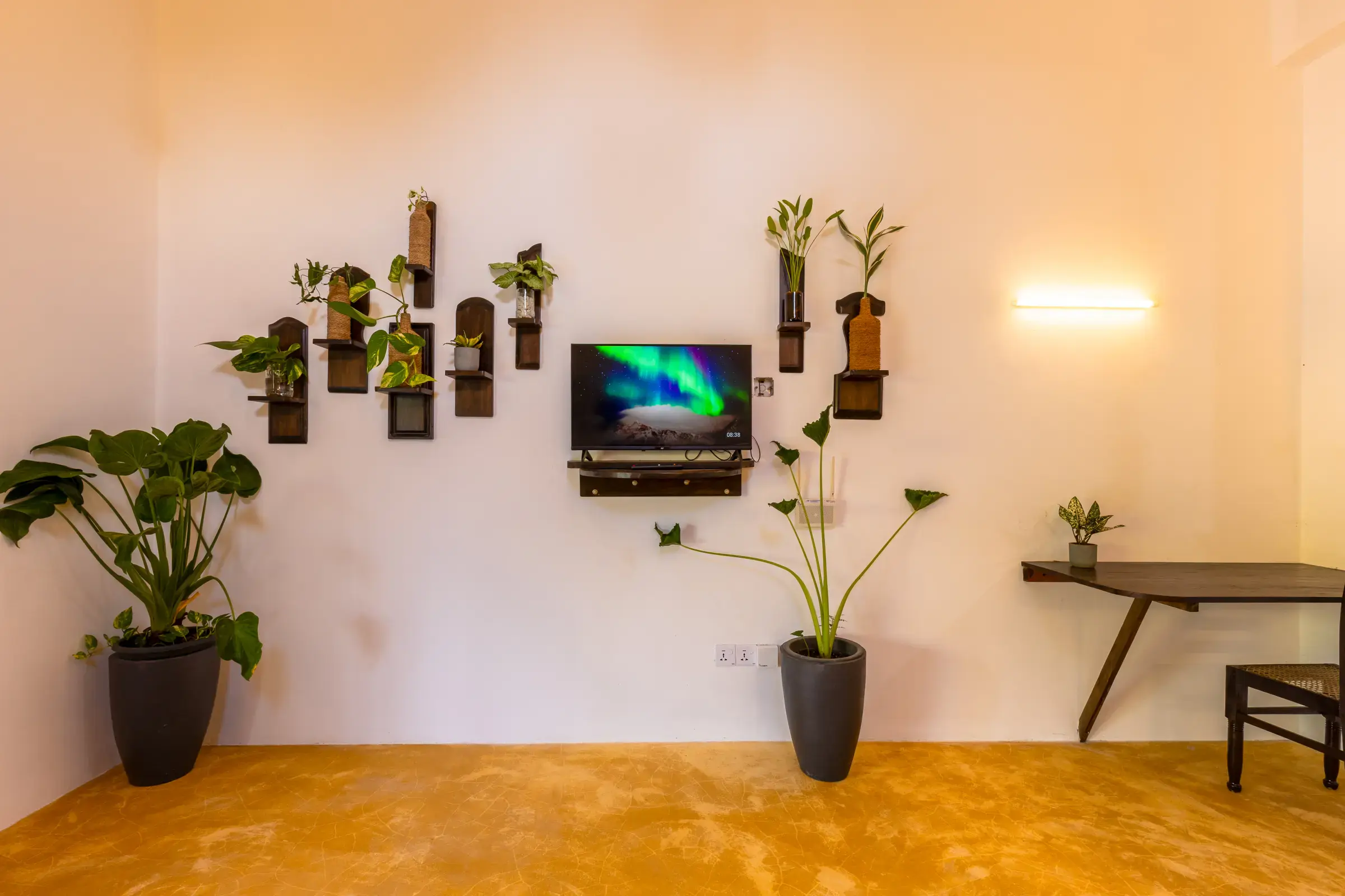Quiet TV lounge with wall-mounted screen, plant shelves and wooden desk at Serene Luxe Villa